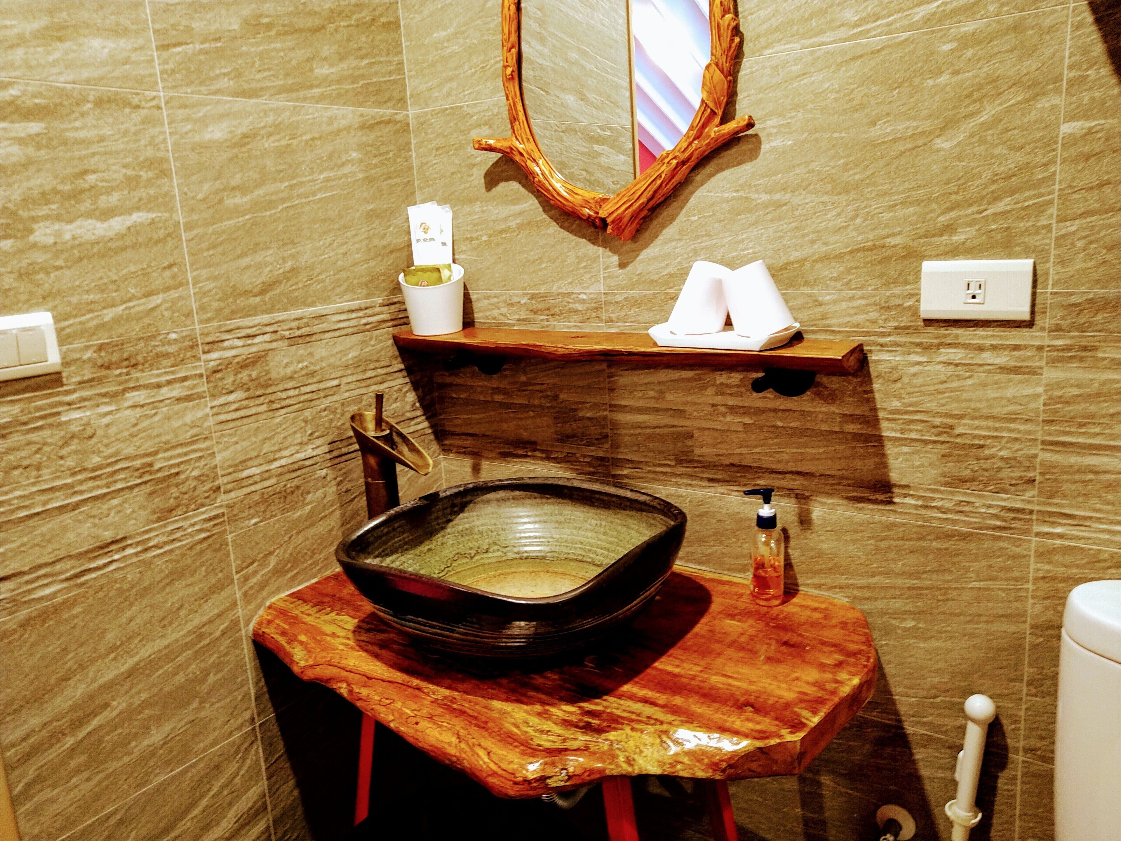 A bathroom with a marble wall, a wooden vanity, a large basin, a mirror, and a towel rack.