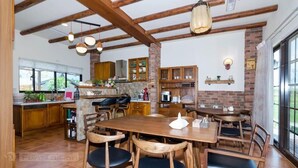 A spacious kitchen with wooden beams, a dining area with a large table and chairs, and a brick wall with shelves. - Celine's B&B (Fenglin)