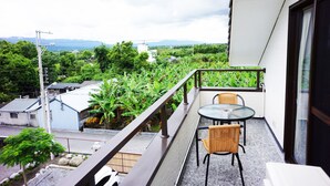 A balcony with a table and chairs, overlooking a lush green landscape and distant mountains. - Celine's B&B (Fenglin)