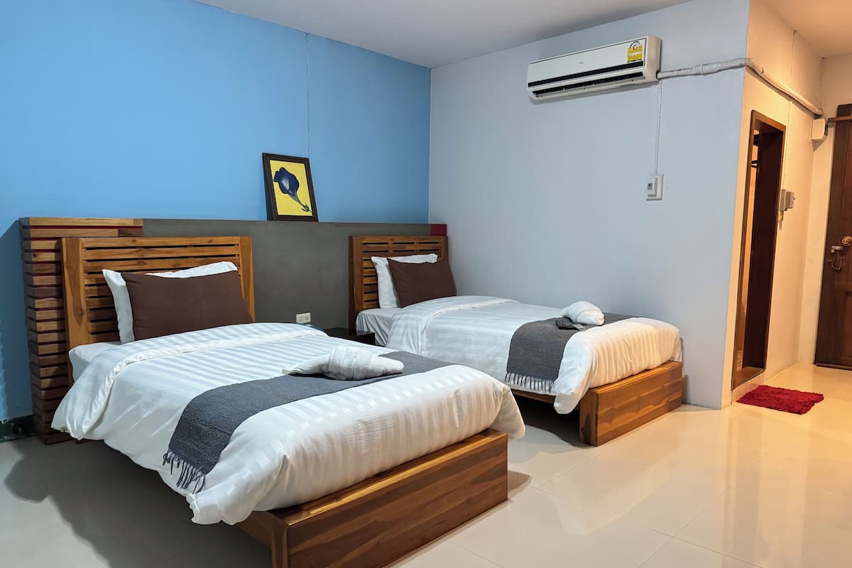 A hotel room with two beds, a wooden headboard, a framed picture on the wall, and an air conditioning unit.