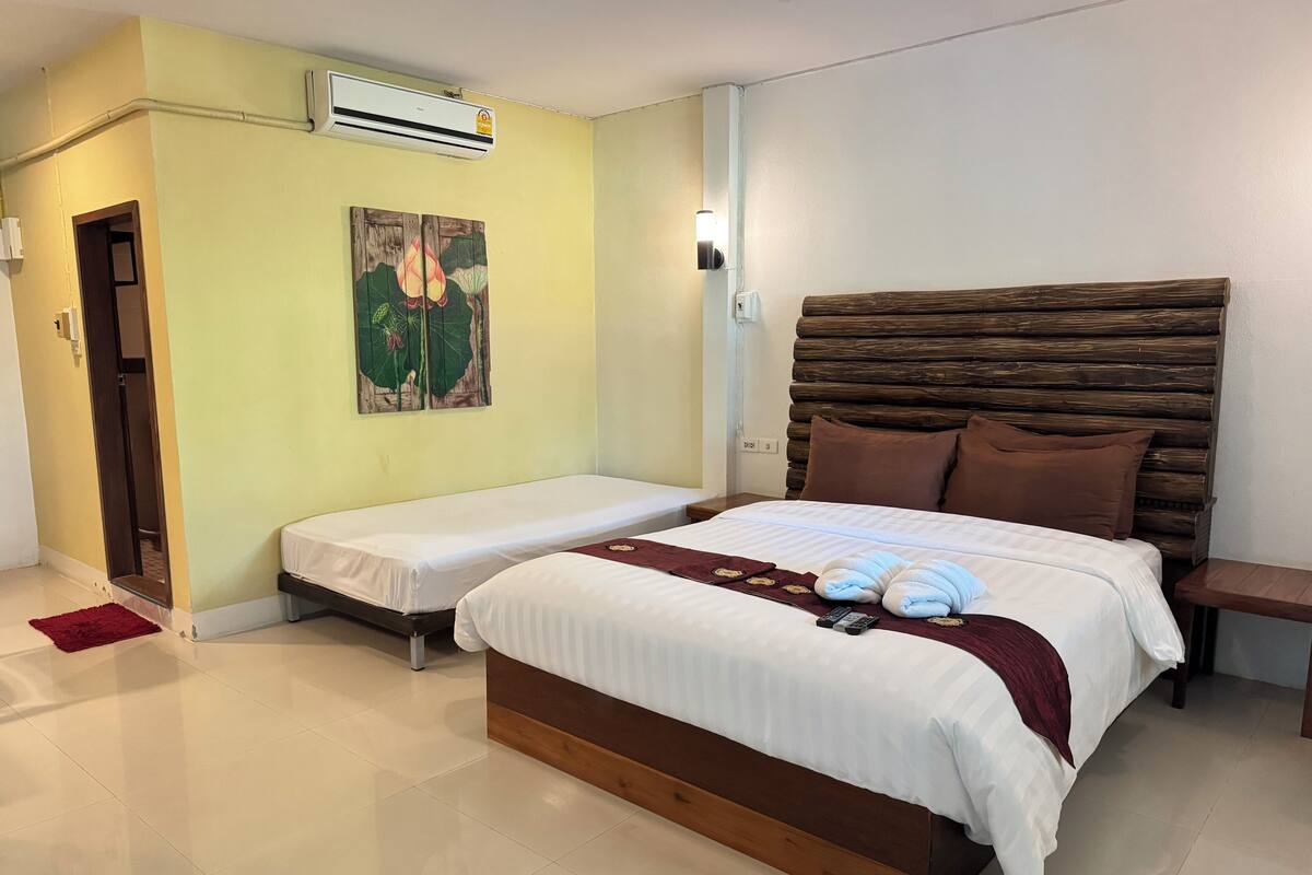 A hotel room with two single beds, a wooden headboard, a wall-mounted air conditioner, and a painting of lotus flowers.