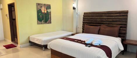 Habitación de hotel con dos camas individuales, cabecera de madera, aire acondicionado de pared y un cuadro con flores de loto.
