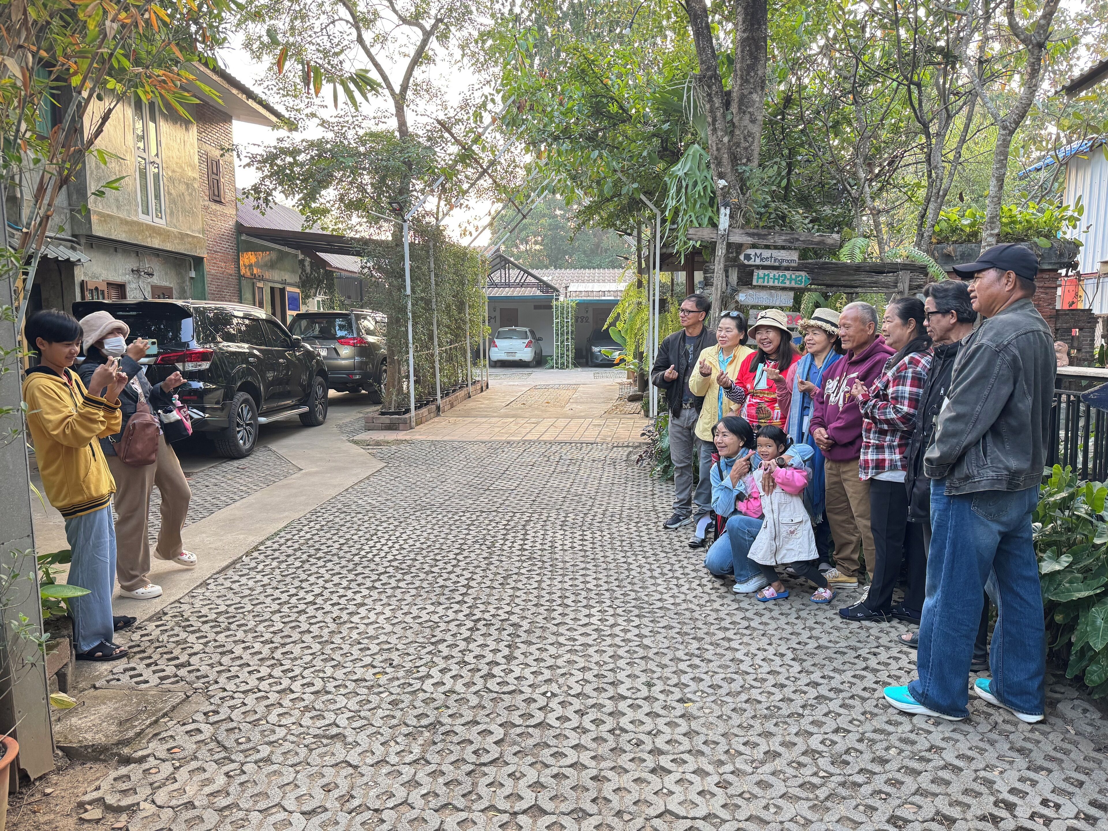 A group of people standing on a paved pathway with a brick pattern, a black SUV parked on the left, and a sign indicating a meeting room.