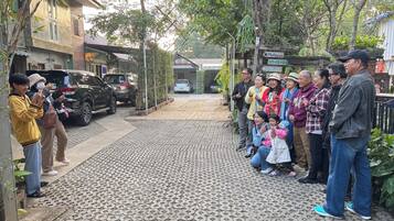 A group of people standing on a paved pathway with a brick pattern, a black SUV parked on the left, and a sign indicating a meeting room.