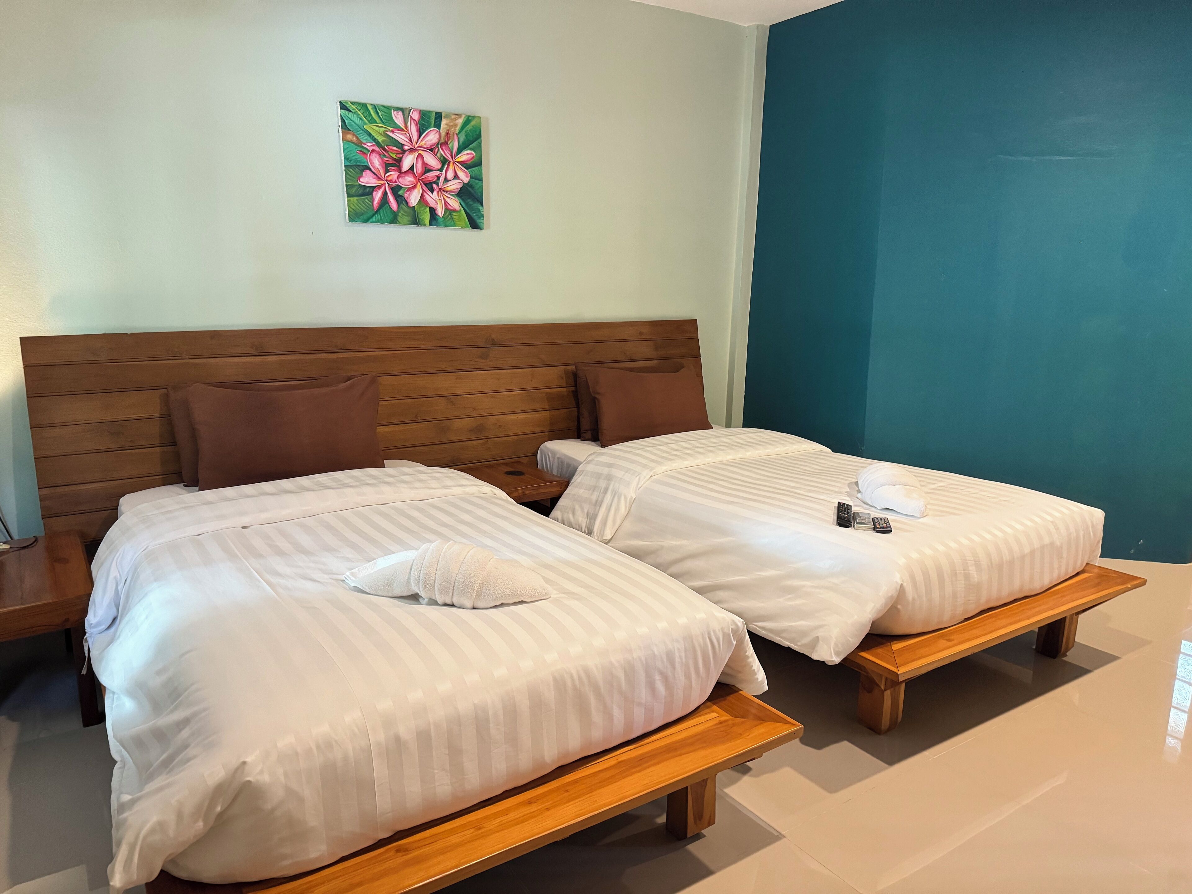 A hotel room with two beds, wooden headboards, and a teal accent wall.