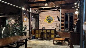 A cozy cafe with wooden furniture, a brick wall with a logo, and a concrete floor. - Ruen Kaew Boutique Resort (Sung Men)