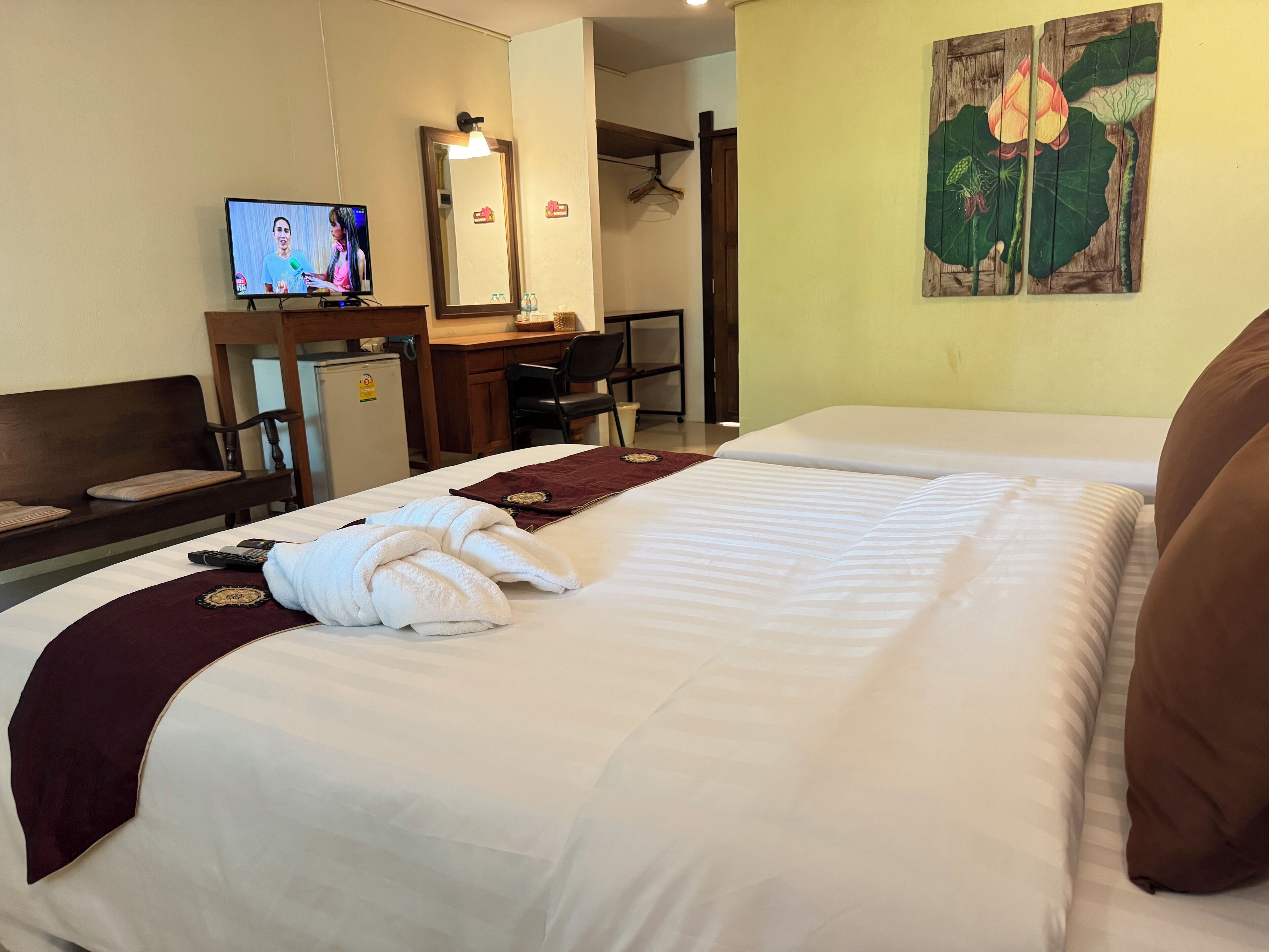 A hotel room with two beds, a desk, a television, a mirror, and a wall painting.
