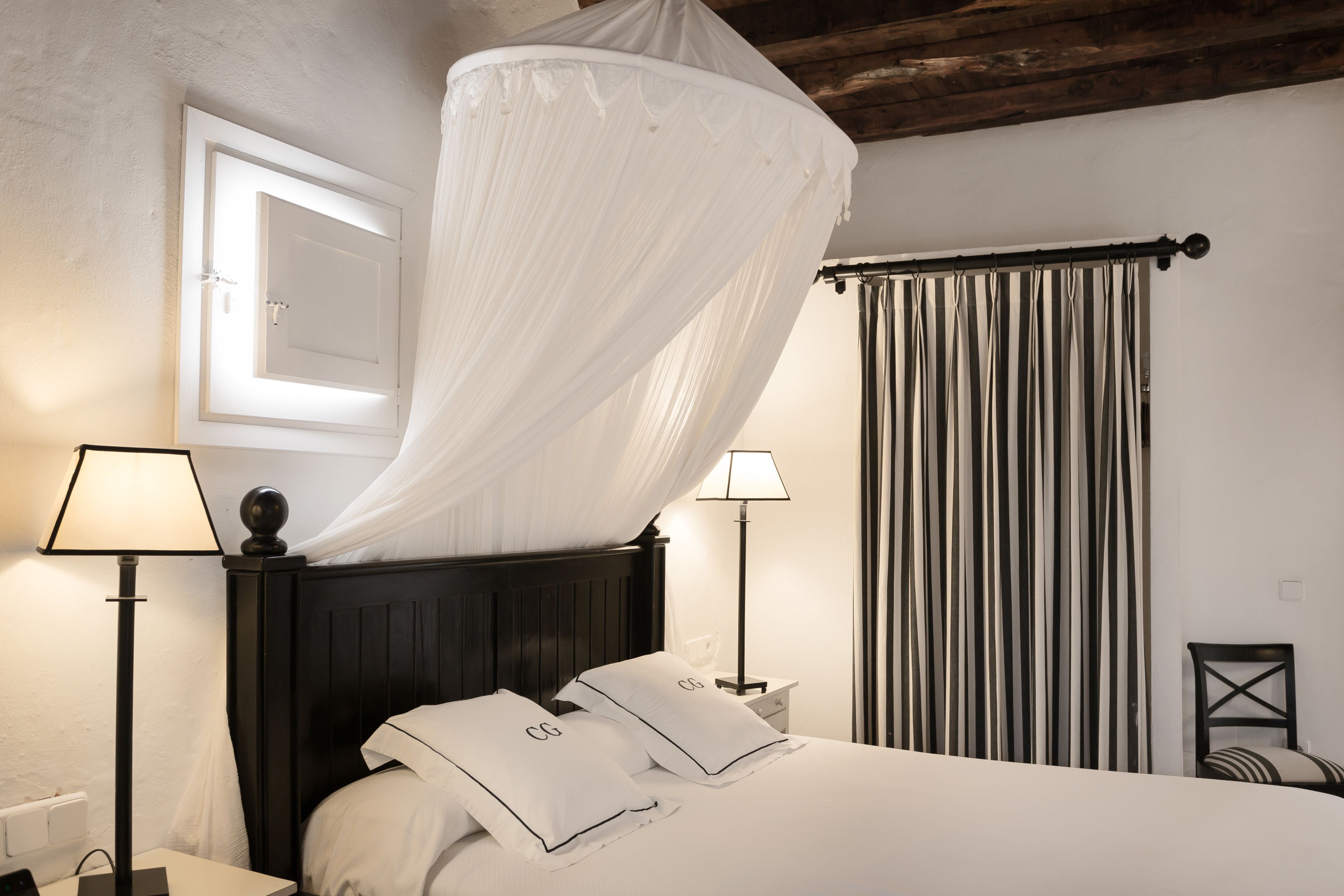 Une chambre à coucher avec un lit, des lampes de chevet, une fenêtre avec des rideaux et une vue sur l’extérieur.