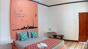 Un dormitorio con cama, almohadas, una mesita de noche y un mural de horizonte urbano en la pared.
