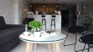 A modern hotel lobby with a reception desk, bar stools, a sofa, and a round glass table with a plant and books. - Robin Hotel Danang (Da Nang)