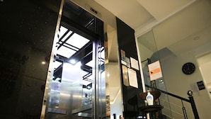 An elevator interior with a digital display, glass doors, and a clock on the wall. - Robin Hotel Danang (Da Nang)