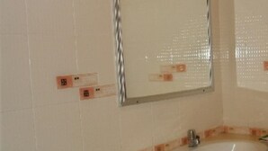 Et badeværelse med en hvid vask, et spejl og en flisebelagt væg med orange detaljer.