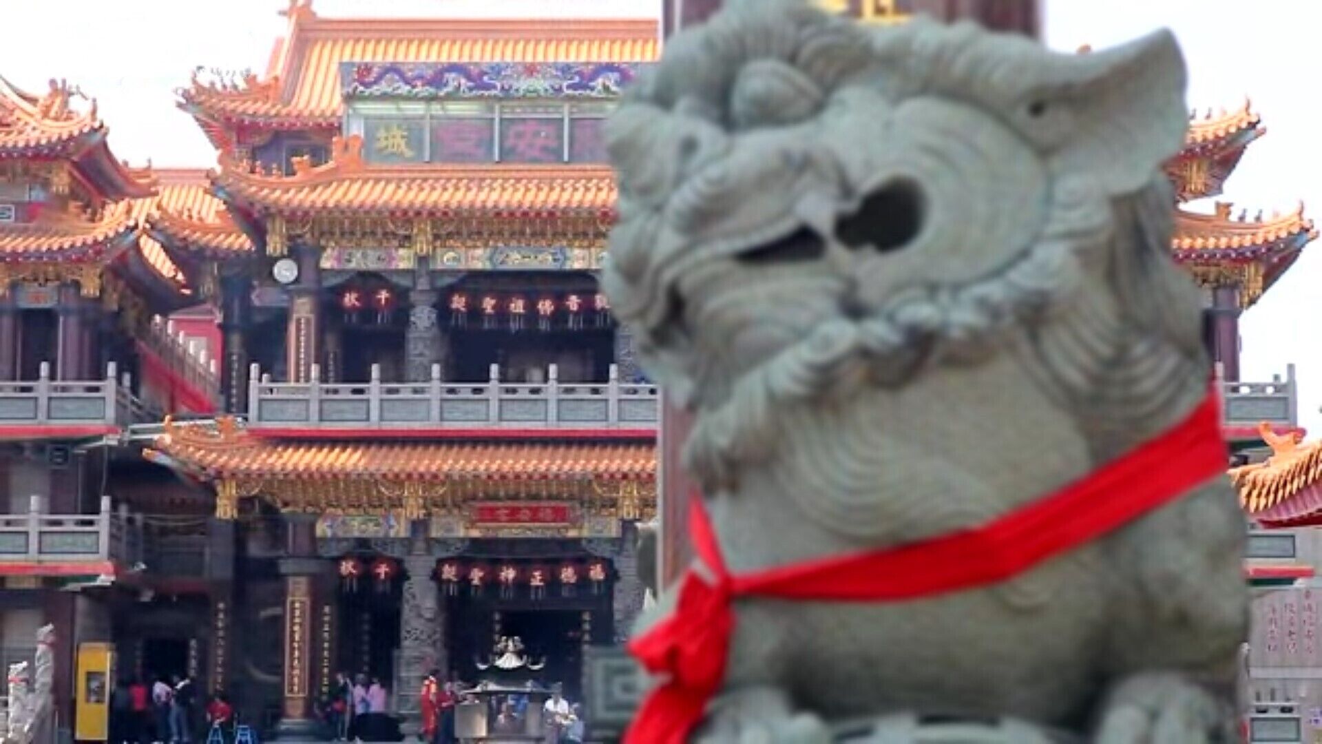 A stone lion statue in front of a traditional Chinese building with ornate architecture.