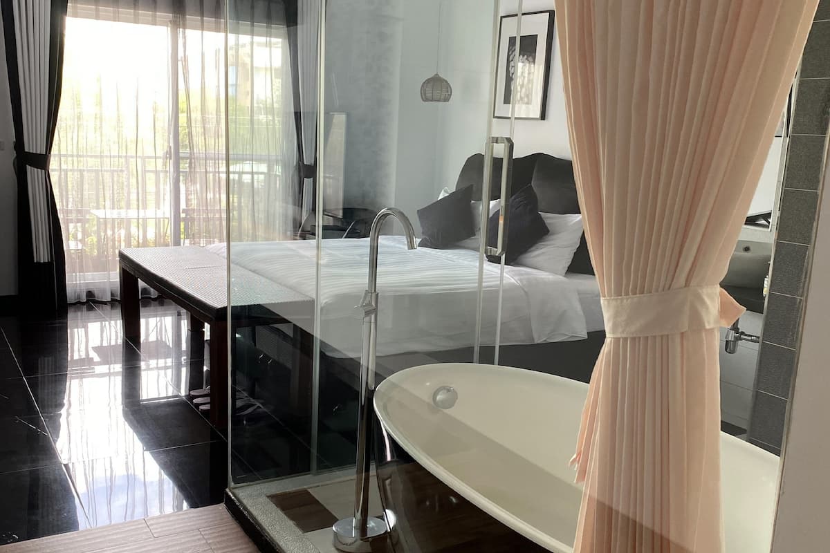 Una habitación de hotel moderna con cama rodeada por cristales, una bañera grande y vistas al exterior.