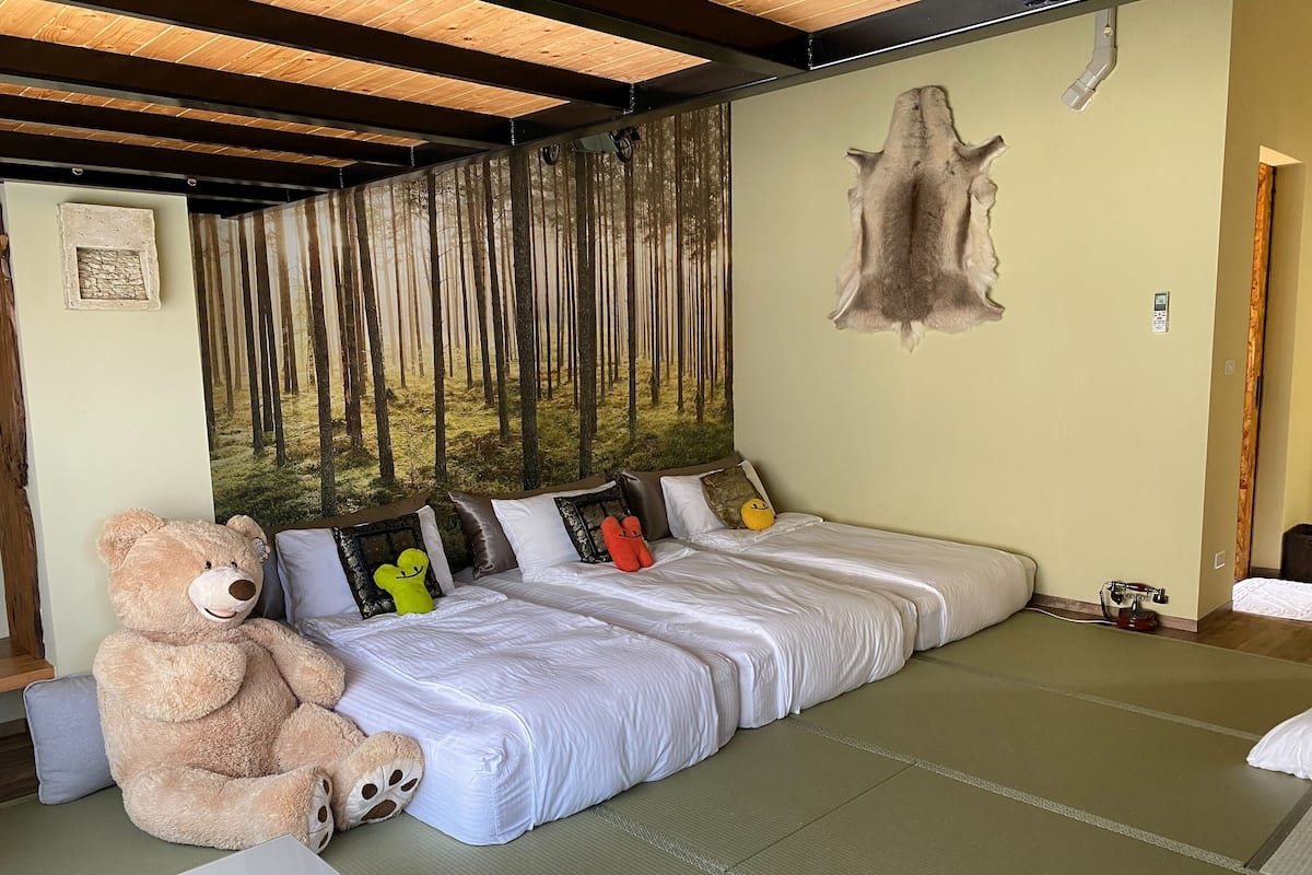 Una habitación con una cama, un oso de peluche grande y un mural de un bosque en la pared.