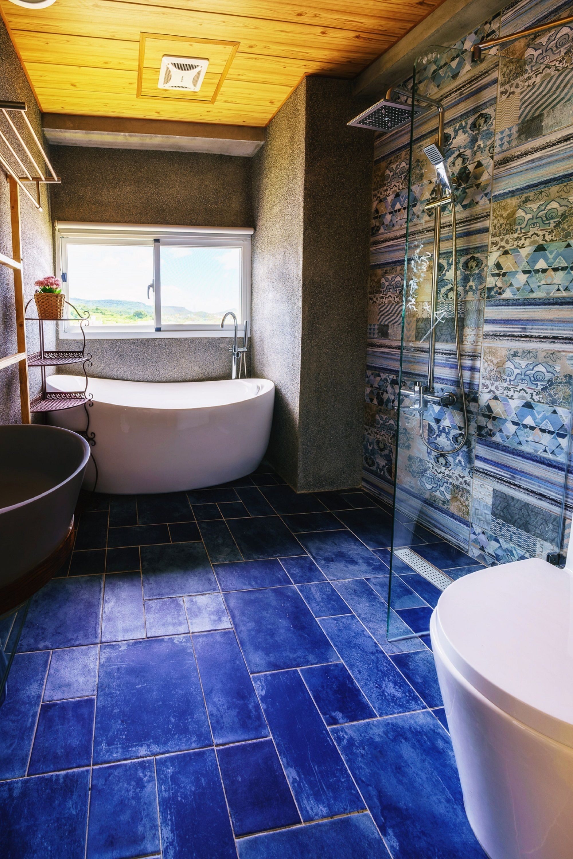 A bathroom with a freestanding bathtub, a glass-enclosed shower, and a window providing a view of the outdoors.