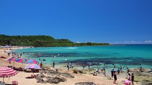 A beach with clear turquoise waters, people swimming and sunbathing, and colorful umbrellas. - La Fleur B&B (Hengchun)