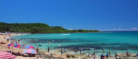A beach with clear turquoise waters, people swimming and sunbathing, and colorful umbrellas.