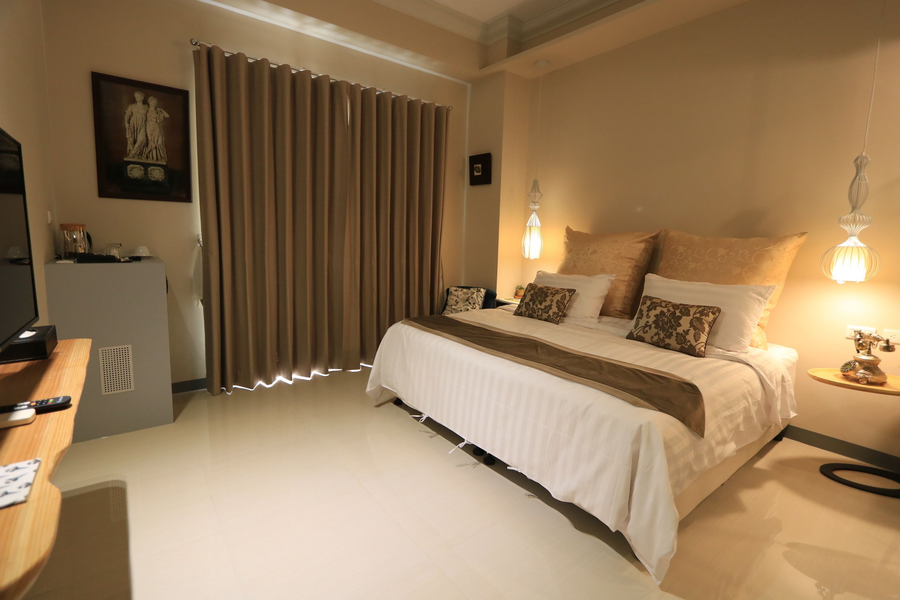 Une chambre à coucher avec un lit, des rideaux, une table de chevet, une lampe et un téléviseur.