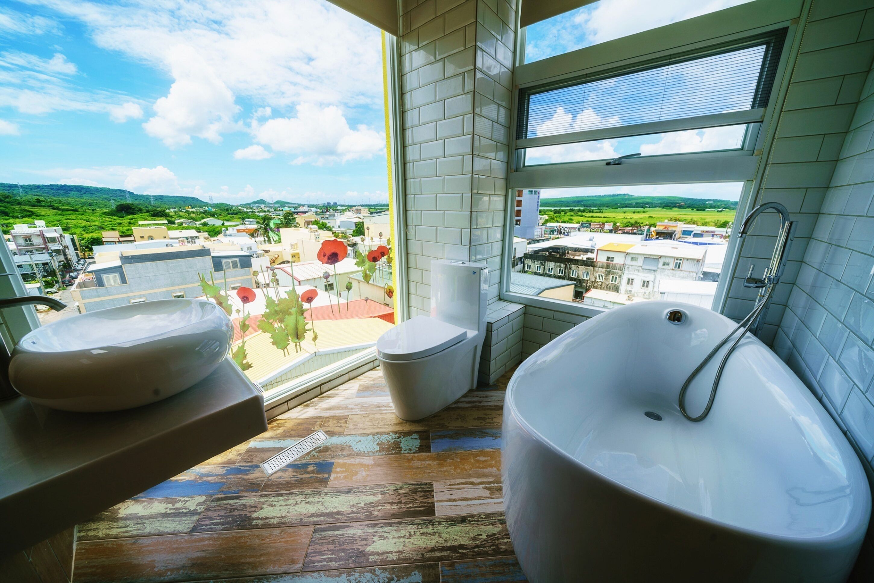 Une salle de bain dotée d’une grande baignoire, de deux lavabos et de toilettes. Elle dispose d’une grande fenêtre offrant une vue sur le paysage urbain et la verdure environnante.
