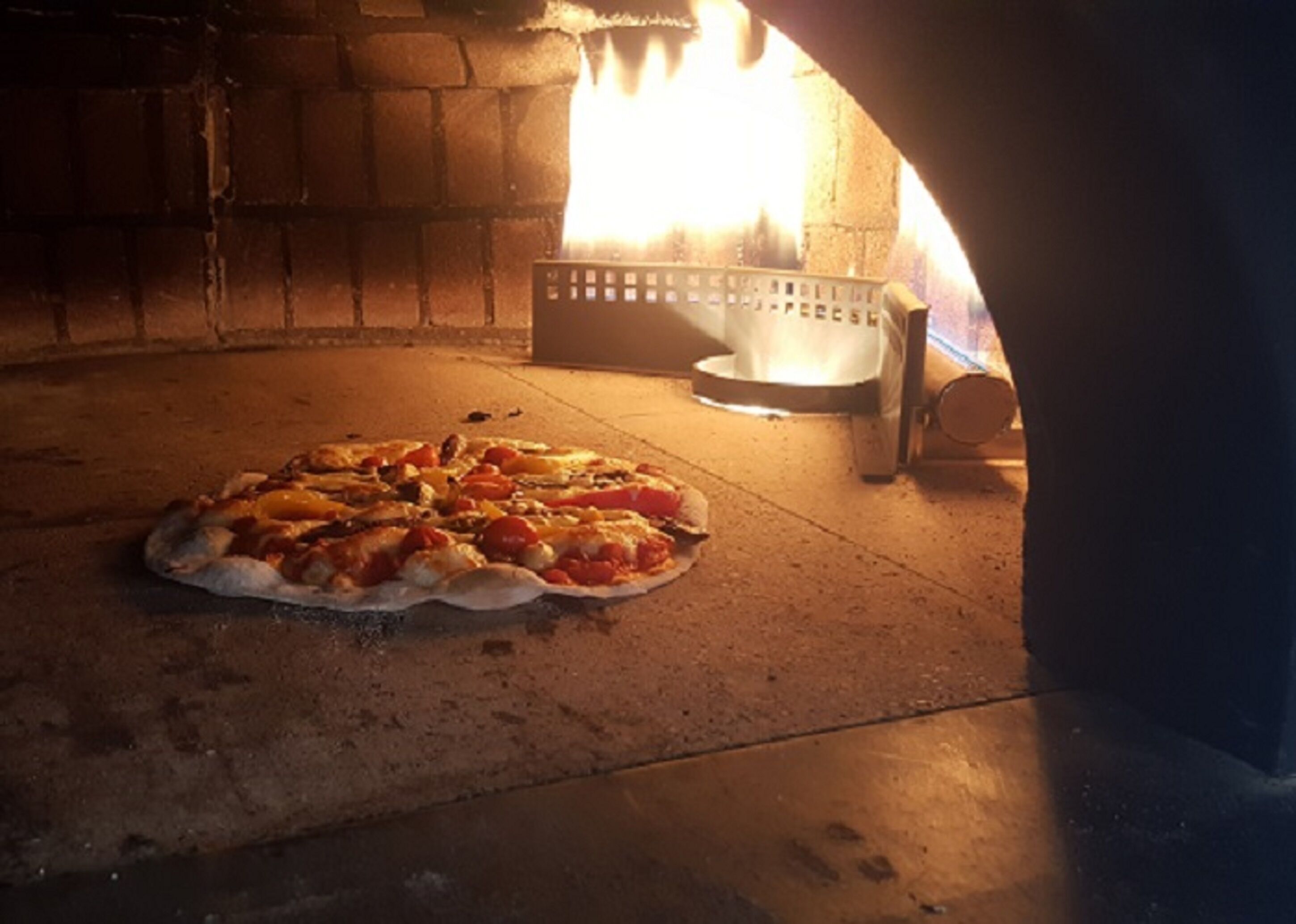 A pizza in a brick oven with flames visible in the background.