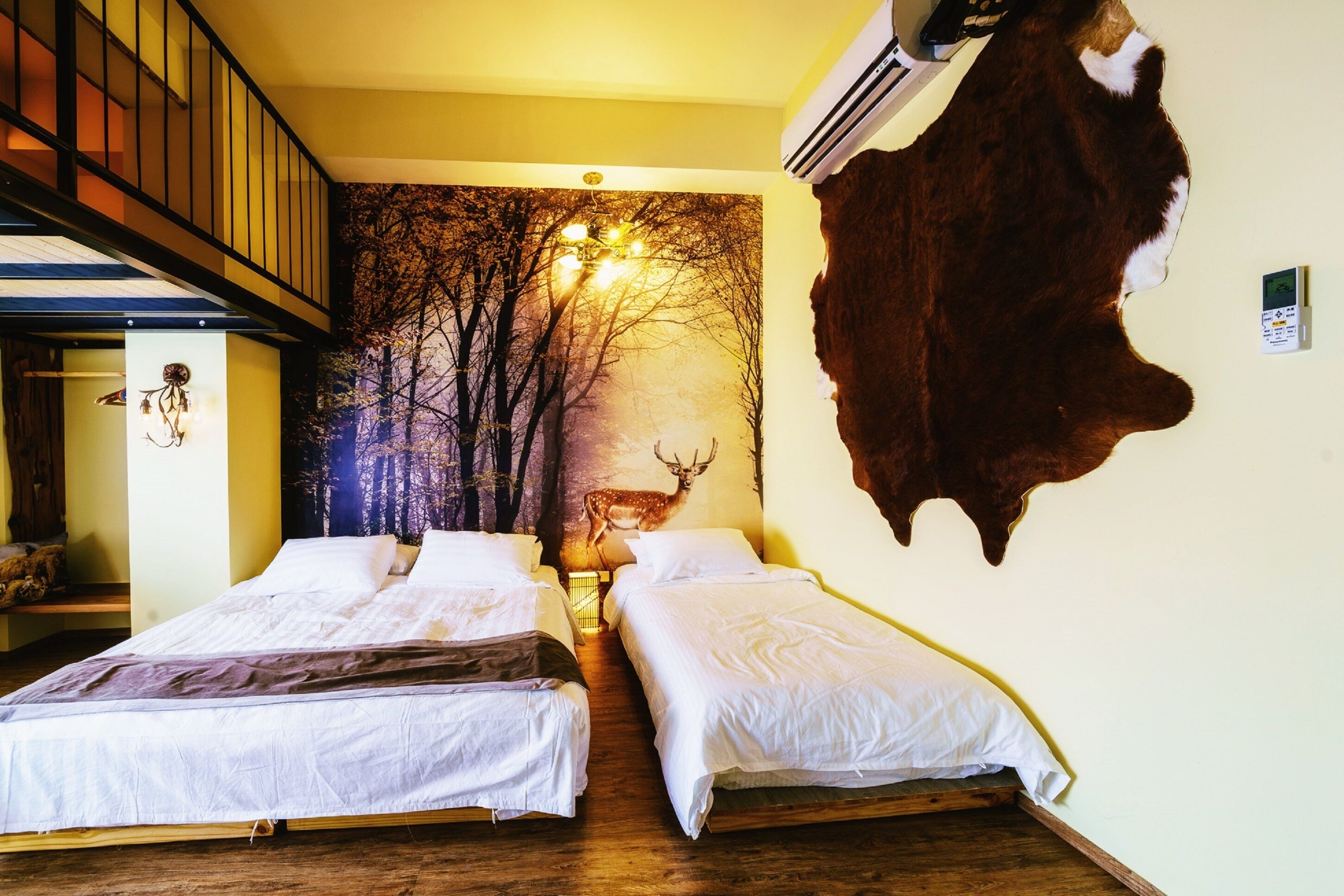 Ein Zimmer mit zwei Betten, Holzboden, einer Wandmalerei zum Thema Wald, einem aufgehängten Tierfell und einer Treppe.