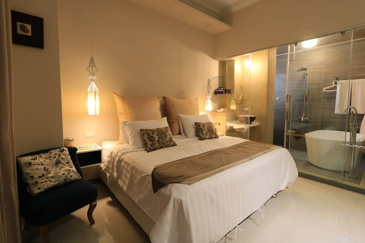 Un dormitorio moderno con una cama grande, mesitas de noche, una silla y una zona de ducha con paredes de vidrio.