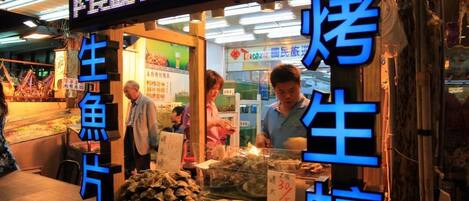 A seafood stall with a neon sign, displaying various seafood items for sale.