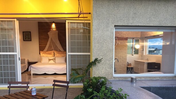 A bedroom with a bed, a window, and a bathroom visible through the window. - La Fleur B&B (Hengchun)
