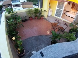 A rooftop patio with potted plants, a seating area, and a view of the surrounding buildings.