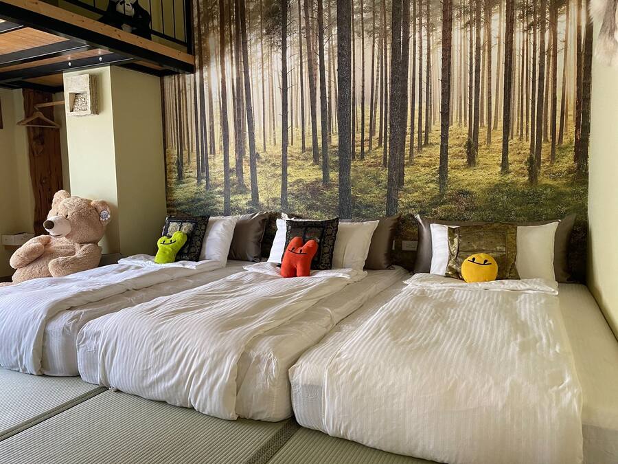 A bedroom with two beds, a large teddy bear, and a forest mural on the wall.