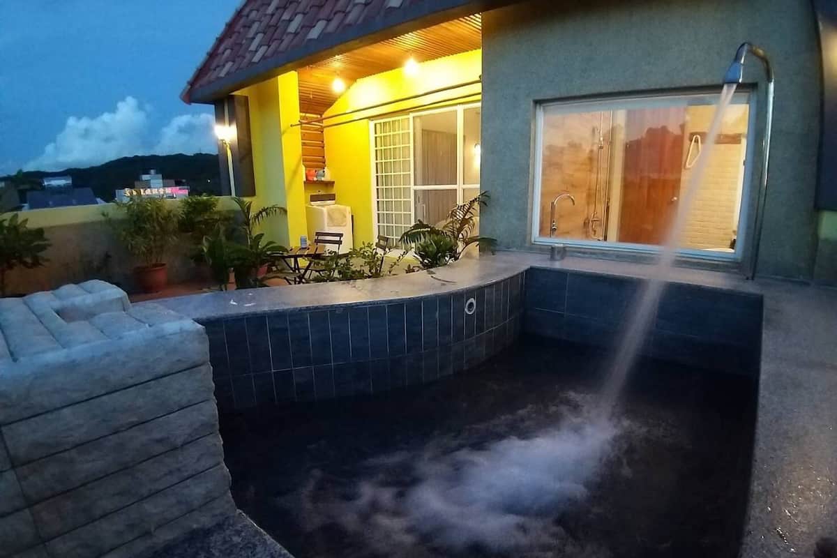 Un área de hidromasaje con piso de baldosas, terraza de madera y zona de estar techada con sillas.