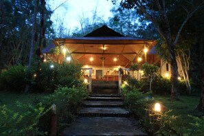 A wooden structure with a thatched roof, surrounded by dense greenery, and illuminated by multiple light sources. - Koh Mook Rubertree Bungalow (Ko Mook)
