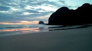 Ein Strand mit einer großen Felsformation und einer entfernten Insel.