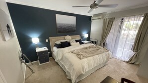 Ein Schlafzimmer mit Bett, Nachttischen, Deckenventilator, Fenster mit Vorhängen und Meerblick.