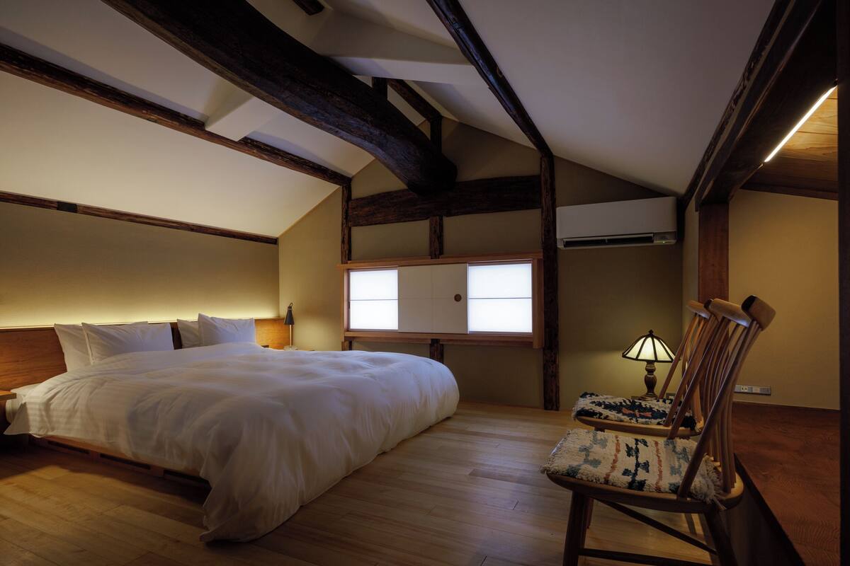Ein Schlafzimmer mit Bett, Stuhl, Fenster und Lampe.