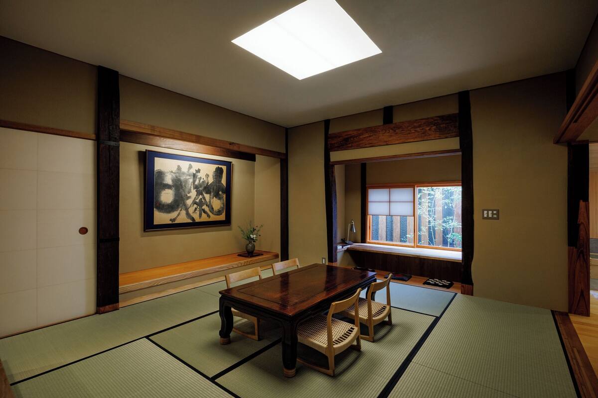 Ein traditioneller japanischer Raum mit Tatami-Bodenbelag, einem Holztisch und einem großen Gemälde an der Wand.