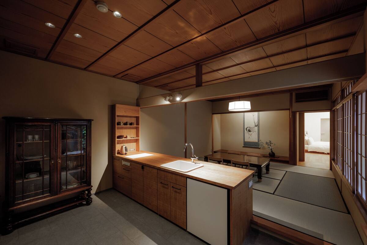 Ein traditioneller japanischer Raum mit Holzbalkendecke, integriertem Waschbecken und einem Sitzbereich mit Tatami-Matten.