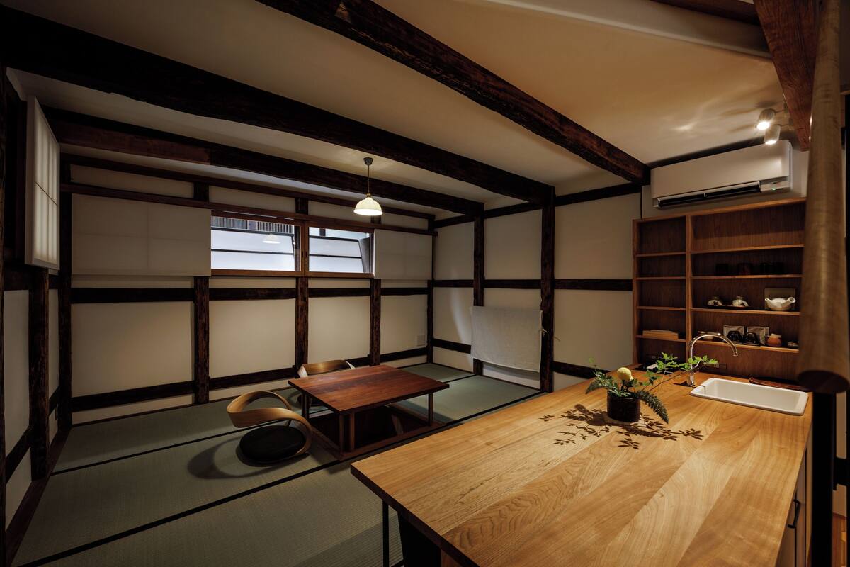 Ein traditioneller japanischer Raum mit Tatami-Bodenbelag, einem Holztisch, einer niedrigen Ablage mit Teeutensilien und einer hängenden Leuchte.