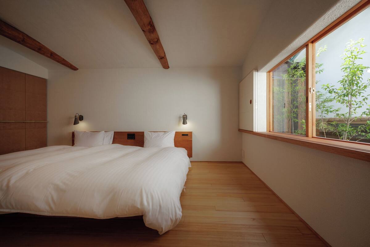 Ein Schlafzimmer mit einem grossen Bett, Holzbalken, einem Fenster mit Aussicht und Nachttischlampen.