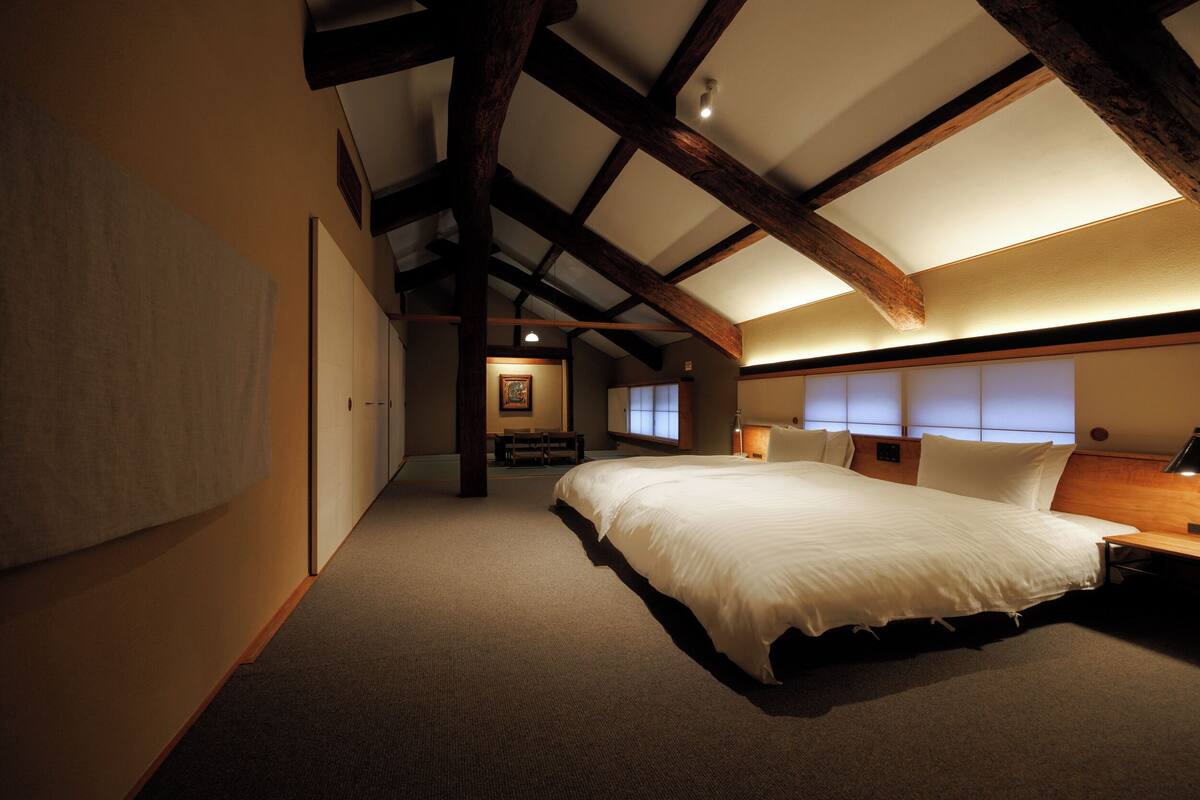 Ein Schlafzimmer mit einem großen Bett, Holzbalken, einer Bank und einem kleinen Tisch.