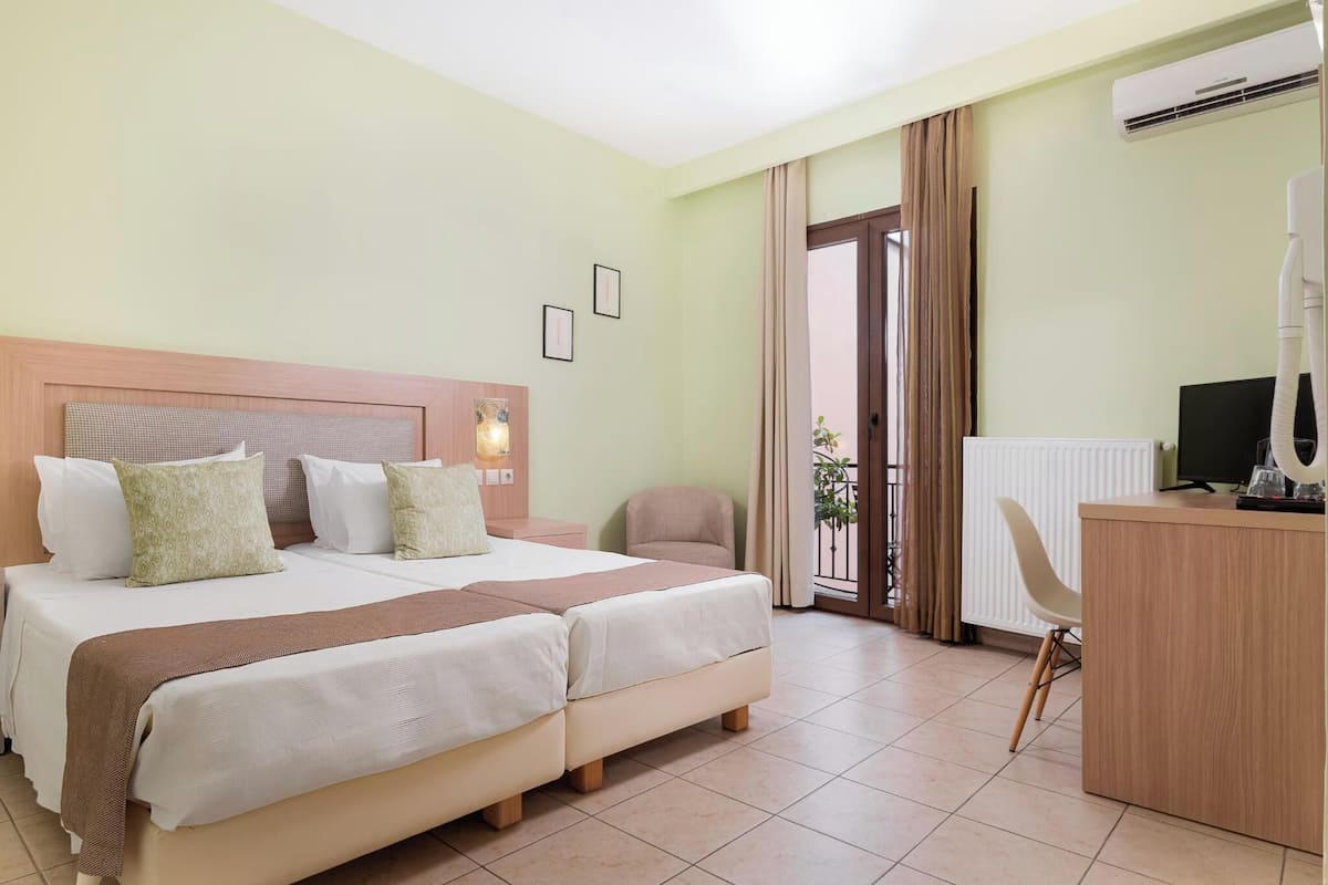 Ein Hotelzimmer mit einem Doppelbett, einem Schreibtisch mit Computer, einem Stuhl und einer Klimaanlage.