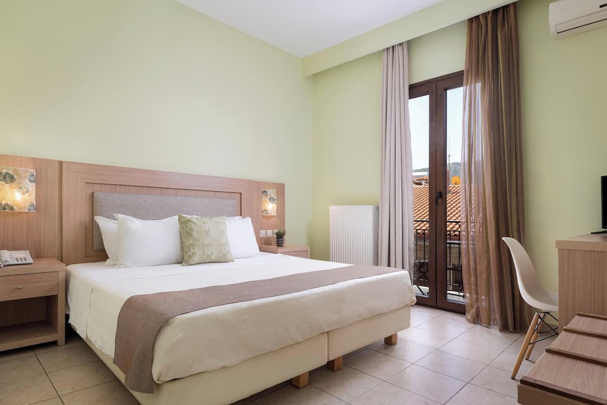 Ein Hotelzimmer mit einem großen Bett, Nachttischen, einem Schreibtisch und Blick auf den Balkon.