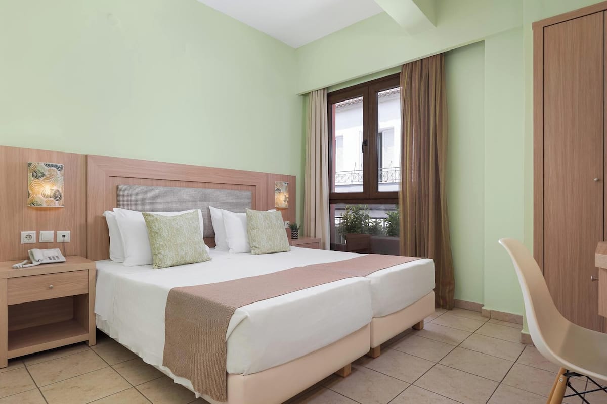 Ein Hotelzimmer mit einem großen Bett, Nachttischen, einem Schreibtisch und einem Fenster mit Vorhängen.
