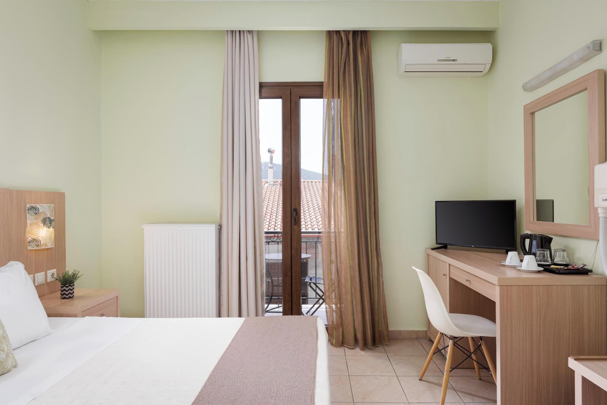 A hotel room with a bed, a desk with a computer, a chair, a window with curtains, and a view of the outside.