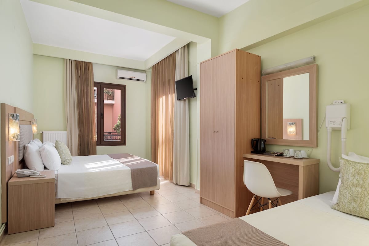 Ein Hotelzimmer mit einem Bett, einem Schreibtisch, einem Stuhl, einem Kleiderschrank, einem Fernseher und einem Badezimmer mit Spiegel und Toilette.