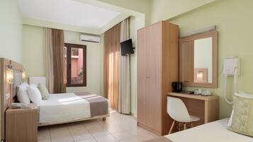 Habitación de hotel con cama, escritorio, silla, armario, televisor y baño con espejo y retrete.