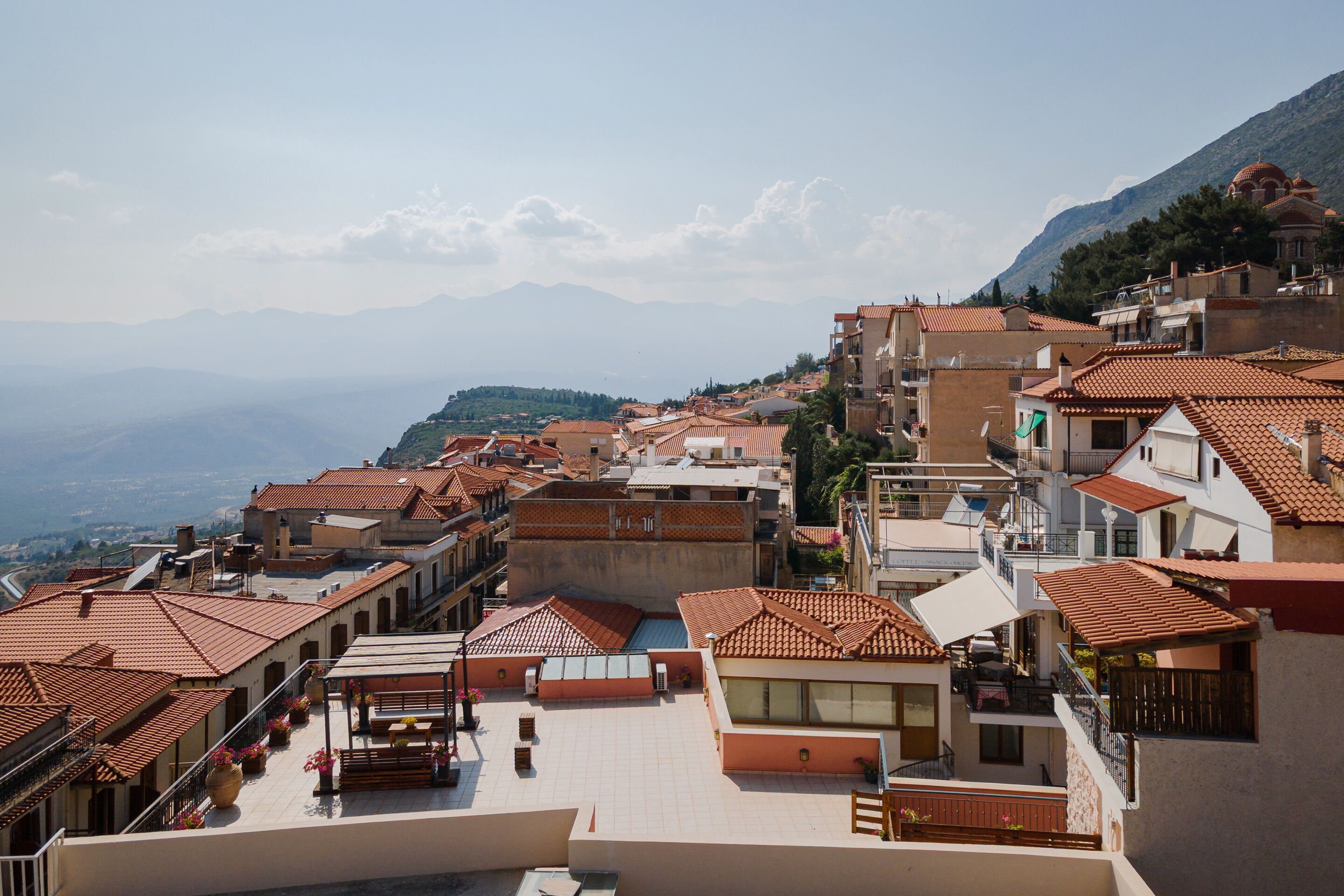 A residential area with terracotta-tiled roofs, balconies, and a mountainous backdrop.