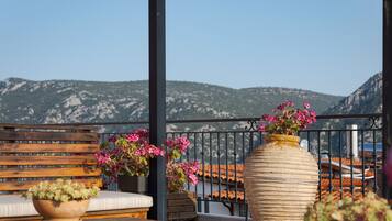 A balcony with a wooden bench, two potted plants with pink flowers, and a large vase.