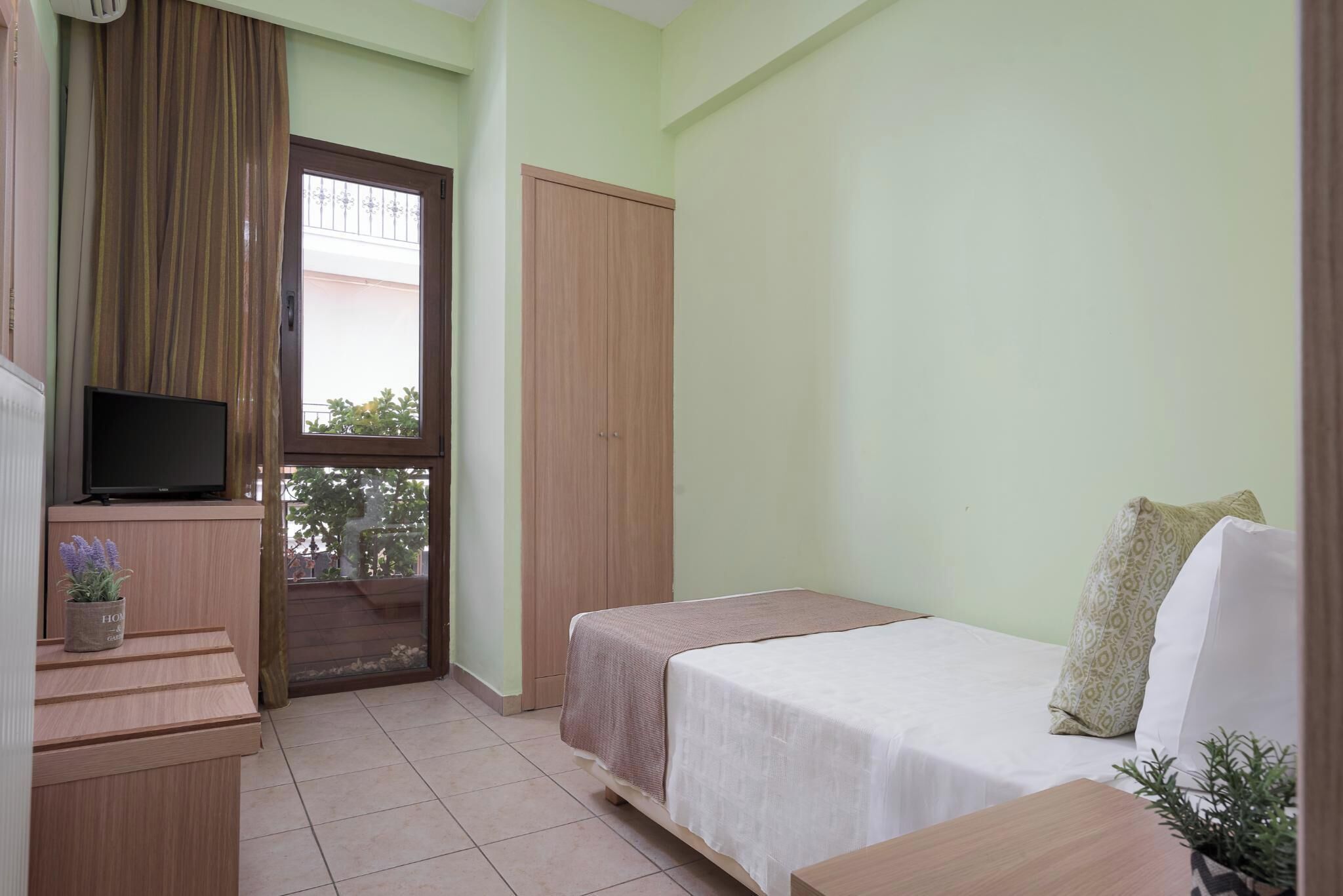 Un dormitorio con una cama, televisión, escritorio y ventana.